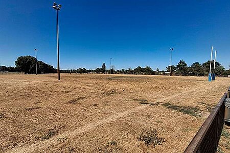 Terrain de football sous un ciel bleu azur avec un grand soleil, avec une pelouse jaunie et clairsem&eacute;e.