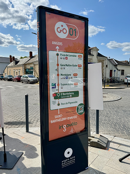 Totem indiquant les temps de trajet : Espace Anjou en 12 min, arrêt de tram Montaigne et 14 min, gare Maître-École en 15 min et le terminus place de Lorraine en 20 min
